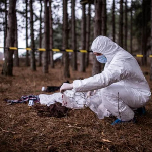 Person in forensic suit examining evidence in a forest scene marked with tape./ppLikely involved in an investigation