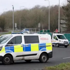 a police van is parked on a road with police tape and a barrier seen in the background.